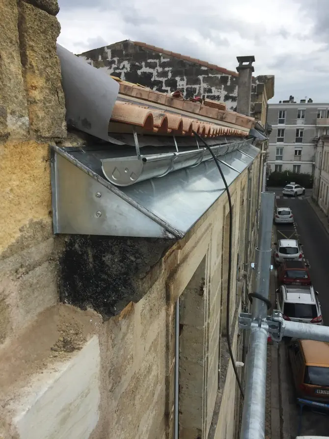 Gouttière et descente en zinc en rive d'immeuble, rue en contrebas