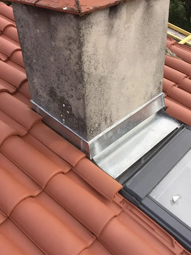 Solin en zinc neuf au pied d'une souche enduite, près d'une fenêtre de toit
